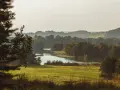 Malowniczy krajobraz Kaszubskiego Parku Krajobrazowego: jezioro, zielone pola i zalesione wzgórza w letnim słońcu.