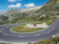 Una moto attende su un tornante del Grimsel Pass, tra montagne verdi e cielo azzurro.