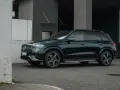 Elegancki, ciemnozielony Mercedes GLE 2025 zaparkowany przed nowoczesnym budynkiem.