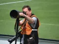 Fotograf z profesjonalnym sprzętem, w tym z długim obiektywem i **monopodem**, gotowy do uchwycenia akcji na boisku.
