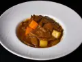 Un delicioso estofado de ternera con trozos de zanahoria y patata en una salsa espesa y aromática, servido en un plato blanco.