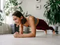 Femme souriante en position de gainage, profitant de son entraînement quotidien à domicile.