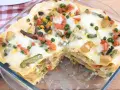 Lasagne di verdure dorate e filanti, con piselli, carote, patate e fagiolini, in una teglia di vetro.