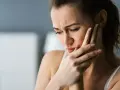 Kobieta z bólem zęba, szuka informacji czym płukać bolący ząb, by ulżyć sobie w cierpieniu.
