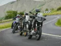 Quattro motociclisti in fila su una strada tortuosa tra colline verdi. Sei motociclista se ami l'avventura.