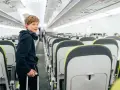 Chłopiec z słuchawkami na szyi i walizką w ręku stoi w przejściu samolotu. Od ilu lat można latać samemu? Ryanair pozwala na samodzielne podróże od 12 roku życia.