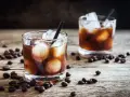 Dwa szklanki z lodem i ciemnym napojem, otoczone ziarnami kawy. Idealny czarny rusek drink na drewnianym blacie.