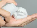 Mano aplicando gel o espuma de afeitar de un envase blanco a la palma.