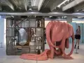 Sculpture rose organique, rappelant l'œuvre de Louise Bourgeois, côtoie une cage métallique remplie de miroirs. Une femme observe l'installation.