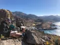 Två personer sitter på en klippa och njuter av utsikten över en by vid havet, inspirerade att måla landskap.