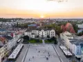 Zachód słońca nad rynkiem, gdzie widać piękną pierzeję kamienic i ratusz. Ludzie spacerują po placu, ciesząc się ciepłym wieczorem.