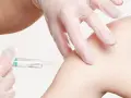 Ręka w rękawiczce wykonuje iniekcję domięśniową w ramię.
