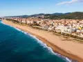 Słoneczna plaża w Malgrat de Mar, z turkusowym morzem i zabudowaniami w tle.