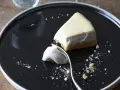 Un trozo de tarta de queso cremoso, con una porción ya probada, sobre un plato negro.