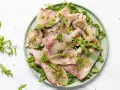 Deliziosi antipasti di pesce crudo, affettati sottili e conditi con erbe aromatiche e olio, serviti su un letto di rucola fresca.