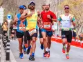 Atleti in gara, con pettorali visibili, corrono su strada. Le tabelle ripetute corsa principianti sono un ottimo modo per iniziare.