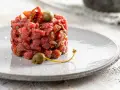 Deliziosa tartare di manzo, guarnita con capperi e pomodori secchi, servita su un piatto grigio.