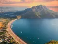 Malownicze wybrzeże Turcji o zachodzie słońca. Góry schodzą do turkusowego morza, a plaża z leżakami i łodziami zaprasza do odpoczynku.