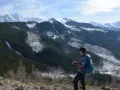 Widok na wielki kopieniec górski pokryty lasem i śniegiem. Kobieta z plecakiem i kijkami trekkingowymi podziwia panoramę.