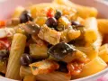 Un piatto invitante di pasta con pesce, arricchito da olive nere, capperi e verdure colorate.