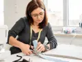 Une couturière utilise des ciseaux pour couper du tissu, montrant l'importance des différents types de ciseaux de couture pour un travail précis.