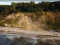 Plaża u stóp najwyższego klifu w Polsce. Ludzie spacerują po piasku, fale obmywają brzeg.