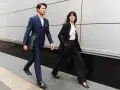 Para idąca w eleganckim business attire, mężczyzna w granatowym garniturze, kobieta w czarnym.