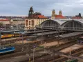 Widok na dworzec kolejowy w Pradze z pociągami na torach i budynkami w tle.