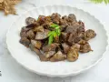 Plato de asadura de cordero salteada, con trozos oscuros y jugosos, adornado con una ramita de perejil fresco.