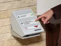 Dłoń naciska przycisk na automacie do wydawania dokumentów rejestracyjnych.