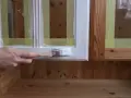 En hand målar en träyta vit med en pensel. Maskeringstejp skyddar intilliggande ytor av furu.