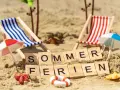 Strandkörbchen, Palmen und die Worte "Sommerferien" im Sand. Perfekt für die Sommerferien in Brandenburg!