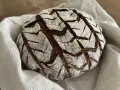Ein rustikales, rundes buchweizenbrot sauerteig mit einer gemusterten Kruste, bestäubt mit Mehl, liegt auf einem weißen Leinentuch.