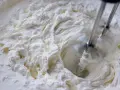 Batidora eléctrica batiendo crema blanca y espesa en un bol.