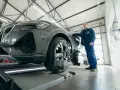 Mechanik w niebieskim kombinezonie stoi obok nowoczesnego samochodu na podnośniku w warsztacie.