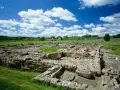 Extensive roman ruin spread across a green field under a blue sky with fluffy clouds.