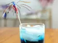Orzeźwiający drink z grenadyną i blue curacao, ozdobiony kolorową parasolką, idealny na letnie popołudnie.