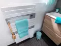 Un sèche-serviettes blanc moderne, avec une serviette turquoise et une brosse de bain en bois. La hauteur du sèche-serviette est idéale pour un accès facile.