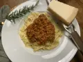 Ein Teller Tagliatelle mit herzhafter Bolognese, garniert mit Rosmarin und Parmesan.