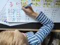 Dziecko rozwiązuje zadania matematyczne. Na kartce widać różne działania, a obok nich cyfry, które mogą stanowić **skalę ocen** lub odpowiedzi.