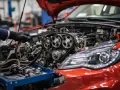 Mechanik w czarnych rękawiczkach dokonuje wymiany łańcucha rozrządu w czerwonym samochodzie.