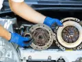 Mechanik w niebieskich rękawiczkach pokazuje zużyte części sprzęgła, które mogą być przyczyną ślizgającego się sprzęgła objawy.