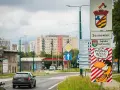 Znak drogowy "Sosnowiec" i humorystyczny napis "Paszport masz?!" przy wjeździe do miasta. W tle bloki mieszkalne.