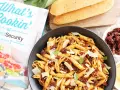 Makaron penne z suszonymi pomidorami, parmezanem i bazylią w czarnej misce, obok pieczywa i książki kucharskiej.