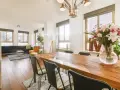 Amplio salón comedor dos ambientes con mesa de madera, sillas negras, sofá, sillones y flores.