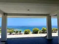 Widok na turkusowe morze z tarasu. W oddali widać małe wysepki i domki z wyjściem na plażę.