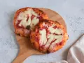 Due pizzette fatte in casa, con pomodoro e mozzarella filante, su un tagliere di legno.