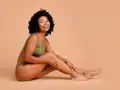 Femme souriante en sous-vêtements verts, caressant sa jambe. Elle partage ses secrets pour comment avoir des pieds doux.
