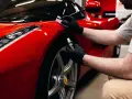 En person med svarta handskar applicerar en skyddande beläggning, troligen **Hydrosilex**, på en röd Ferrari.