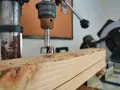 Trapano a colonna che fora un pezzo di legno, creando trucioli. Un esempio pratico di come avvitare una vite nel legno, o meglio, preparare il foro.
